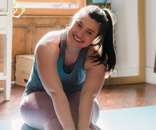 Person smiling while doing a light stretching exercise in a bright room.